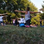 Group of adults practicing yoga outdoors in a park surrounded by trees.