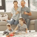 Cheerful family wearing casual clothes sitting in living room while playing and drinking tea during weekend at home in morning